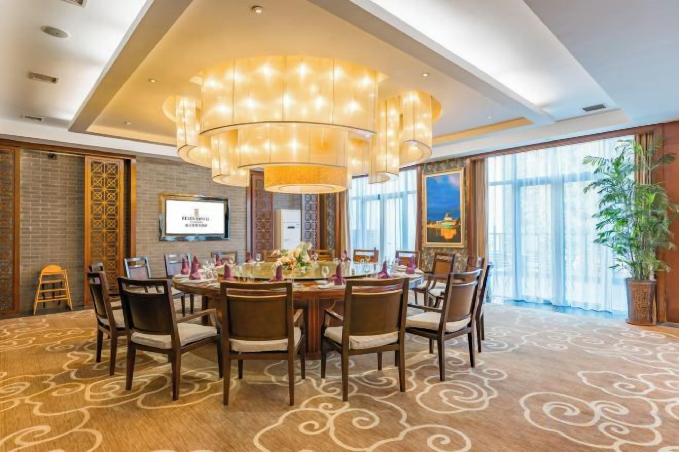 A conference room with a round table, multiple chairs, a large chandelier, and a television screen.