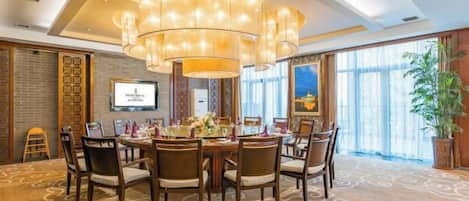 A conference room with a round table, multiple chairs, a large chandelier, and a television screen.
