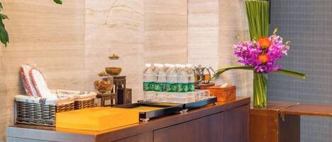 A reception desk with a vase of flowers, bottled water, and a basket of snacks.