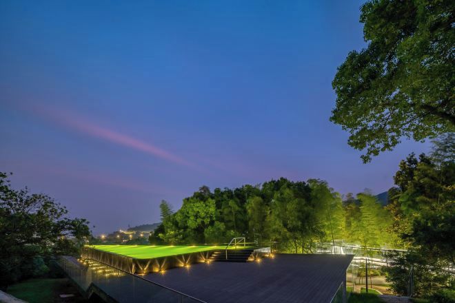 A tennis court with a net and surrounding trees at dusk.