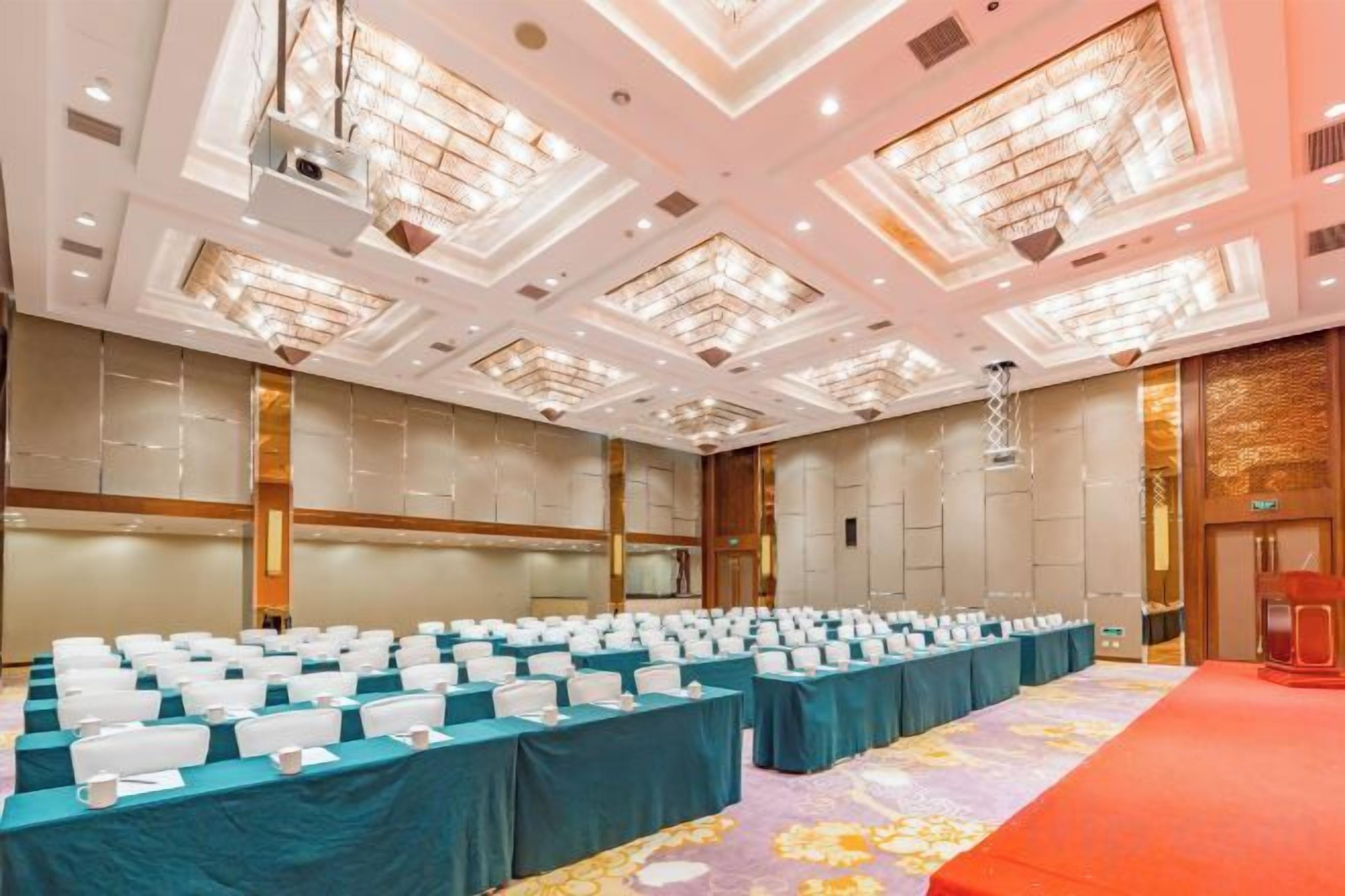 A conference room with rows of tables, a stage, and a red carpet.