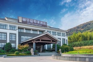 Un hotel con fachada moderna, vestíbulo cubierto y zona ajardinada.