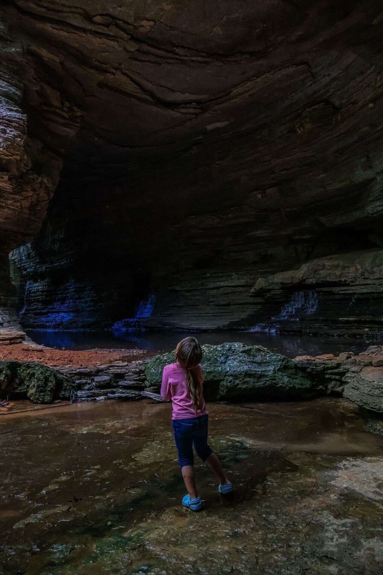 A cave with a small waterfall and a person standing in the water.