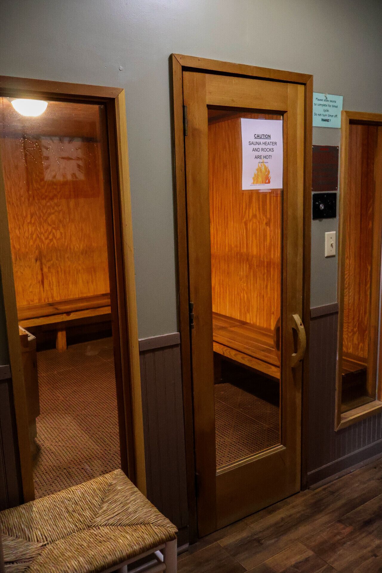 A sauna room with a wooden door, a caution sign, and a bench.