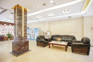 Un hall d’entrée avec une colonne en marbre, des canapés en cuir, une table basse et un comptoir d’accueil.