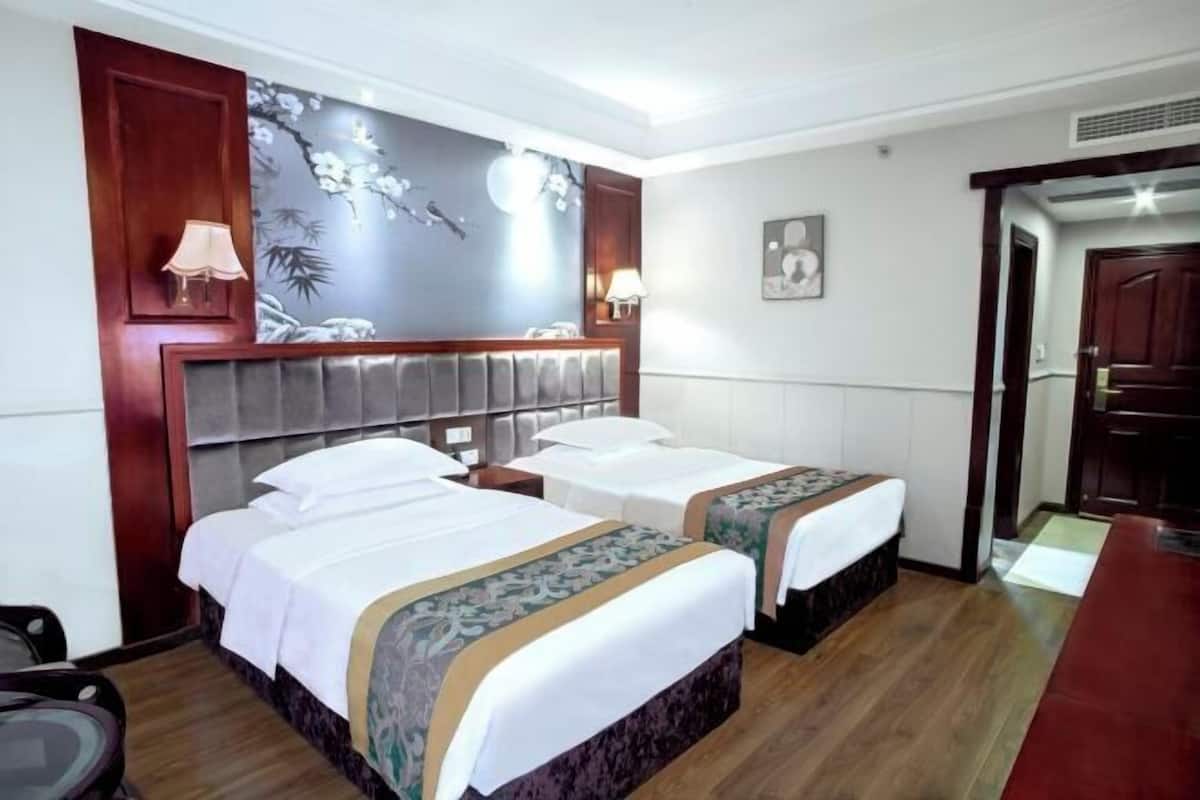 A hotel room with two beds, a wooden headboard, a wall mural, and a small desk.