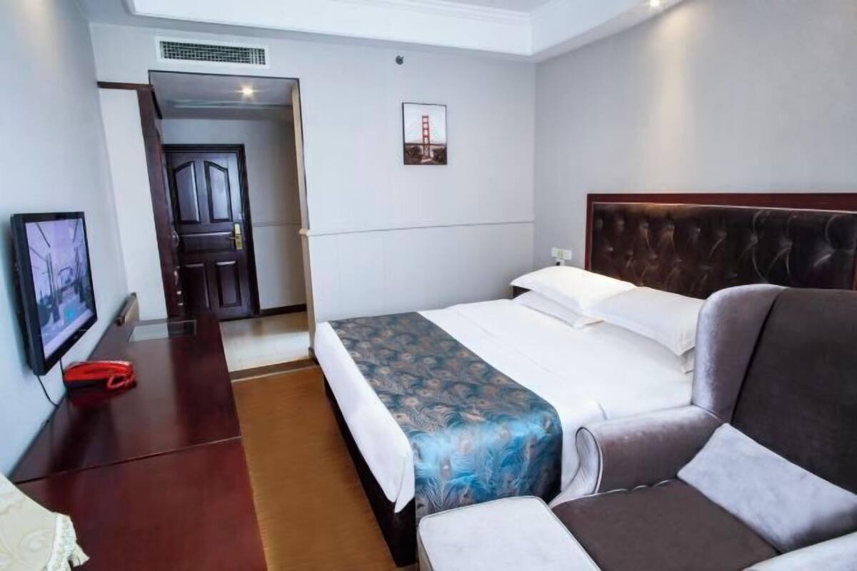 A hotel room with a bed, a chair, a TV, and a door leading to another room.