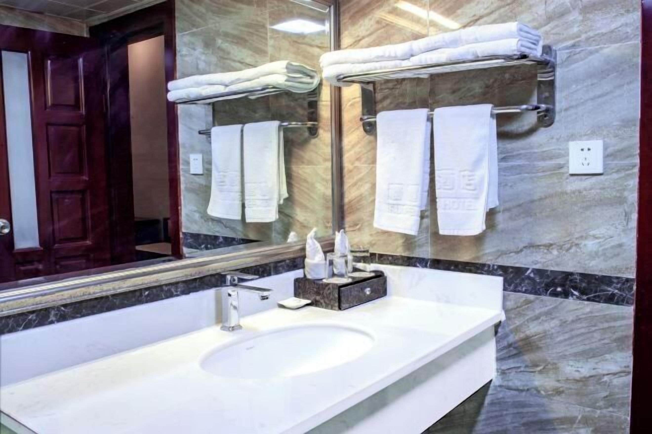 A bathroom with a marble sink, a large mirror, and multiple towels on towel racks.