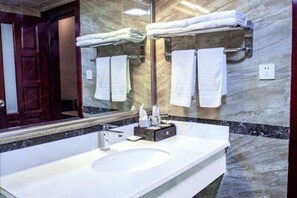Un baño con lavamanos de mármol, un espejo grande y varias toallas en toalleros.