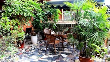 An outdoor patio with a tiled floor, a table with chairs, and various potted plants.
