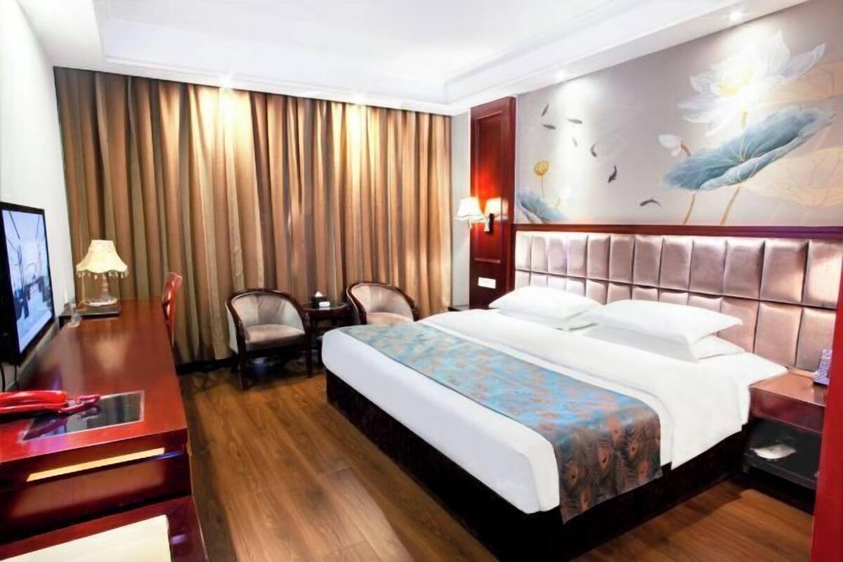 A hotel room with a bed, a desk, a chair, a TV, and a wall with a floral mural.