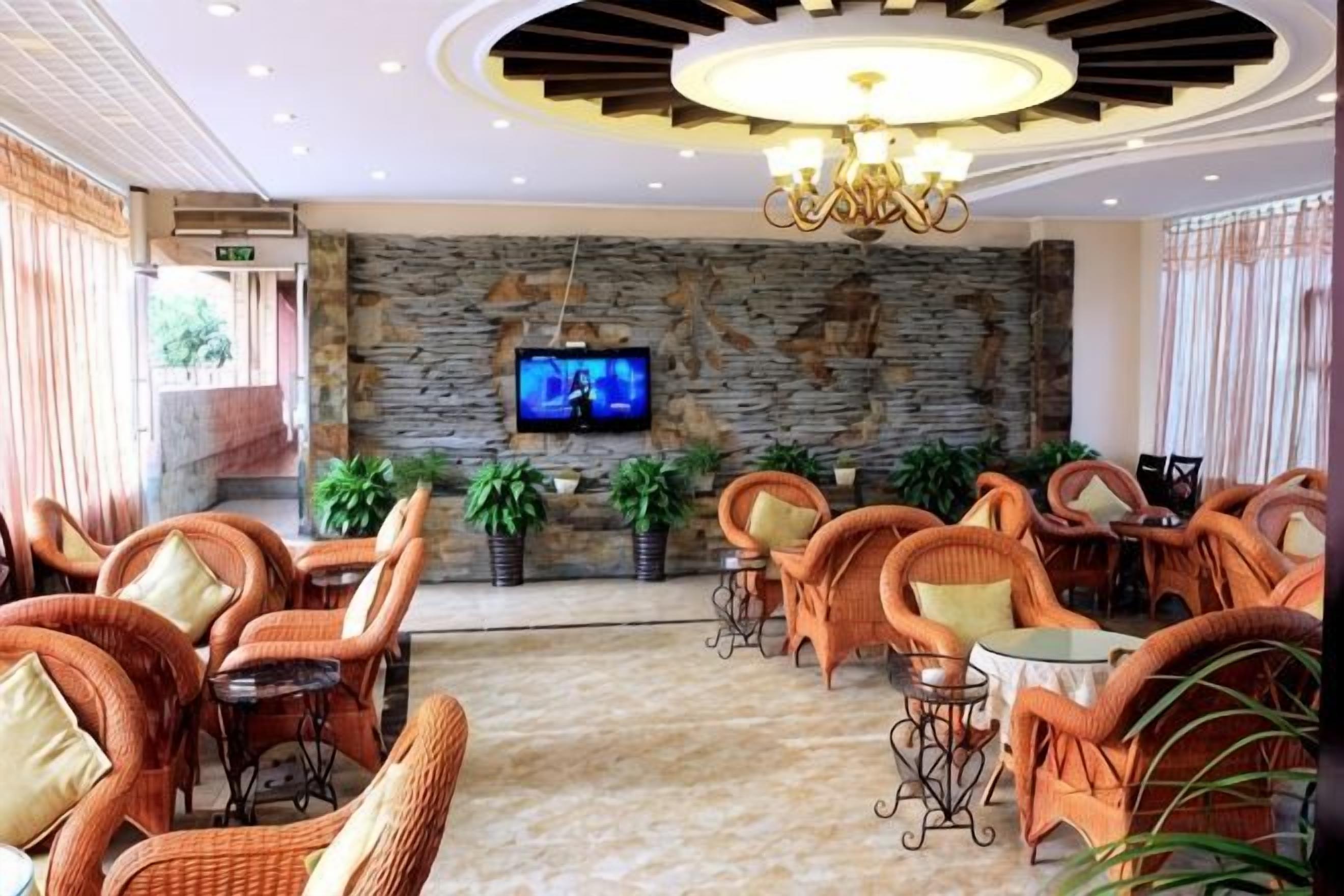 A lobby with wicker furniture, a stone wall, a television, and a chandelier.
