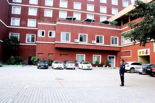 Un edificio de varios pisos con fachada roja, varios autos estacionados y un guardia de seguridad.