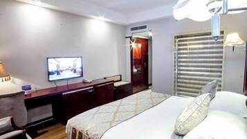 Una habitación de hotel con cama, escritorio, televisión y ventana con persianas.