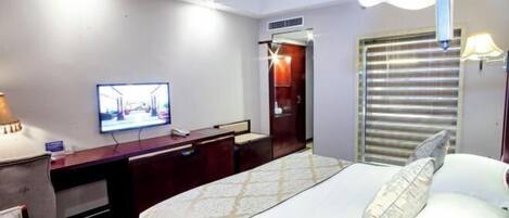 A hotel room with a bed, a desk, a television, and a window with blinds.