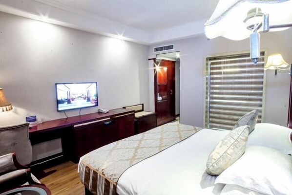A hotel room with a bed, a desk, a television, and a window with blinds.