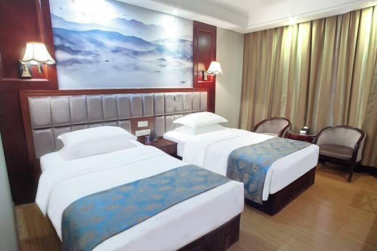 A hotel room with two beds, a headboard, a painting on the wall, a chair, and a lamp.