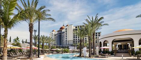 A resort pool area with palm trees, lounge chairs, and umbrellas.