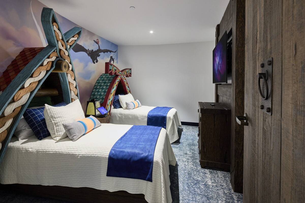 A hotel room with two beds, a wooden wardrobe, a TV, and a mural on the wall.