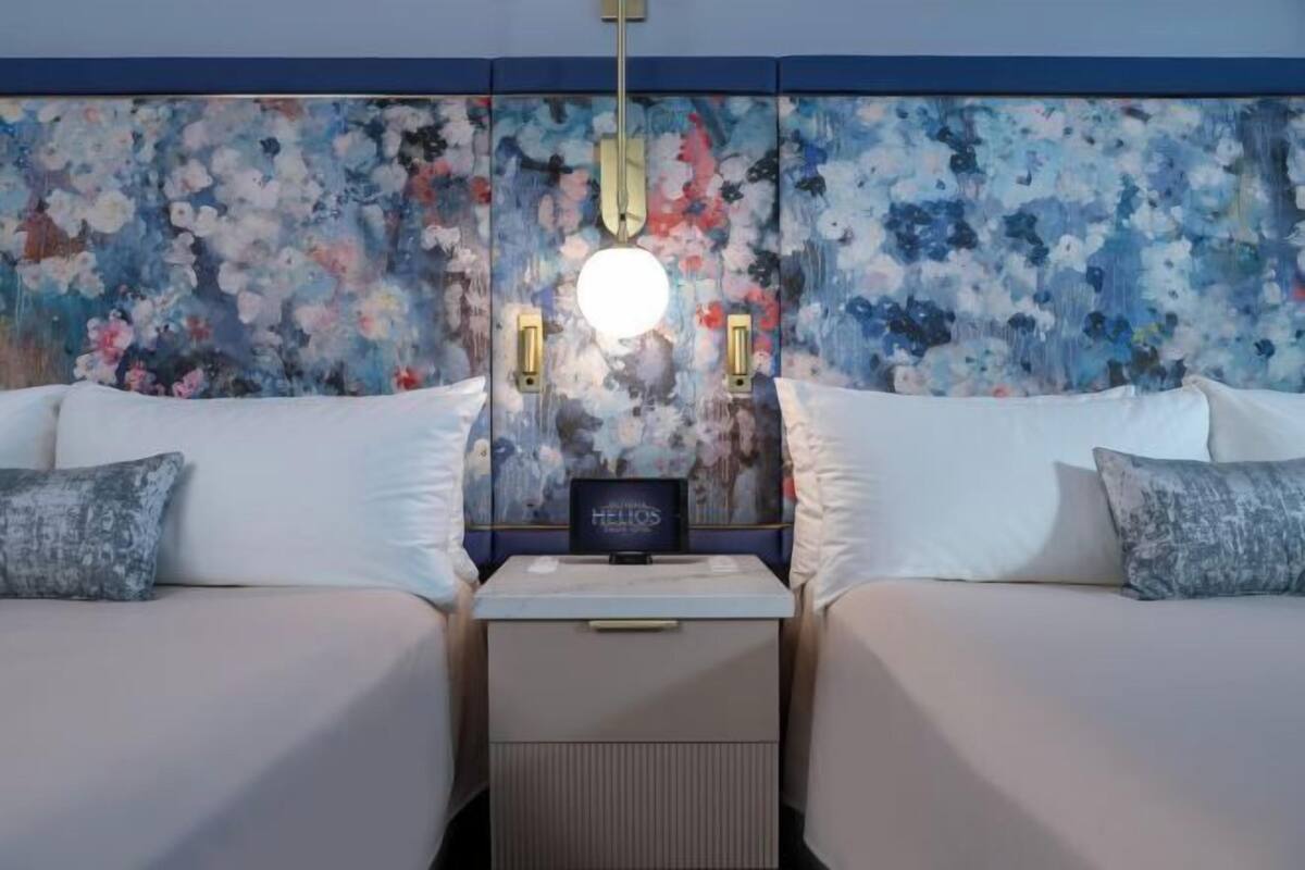 A hotel room with two beds, a nightstand, a decorative wall with floral patterns, and a round ceiling light.