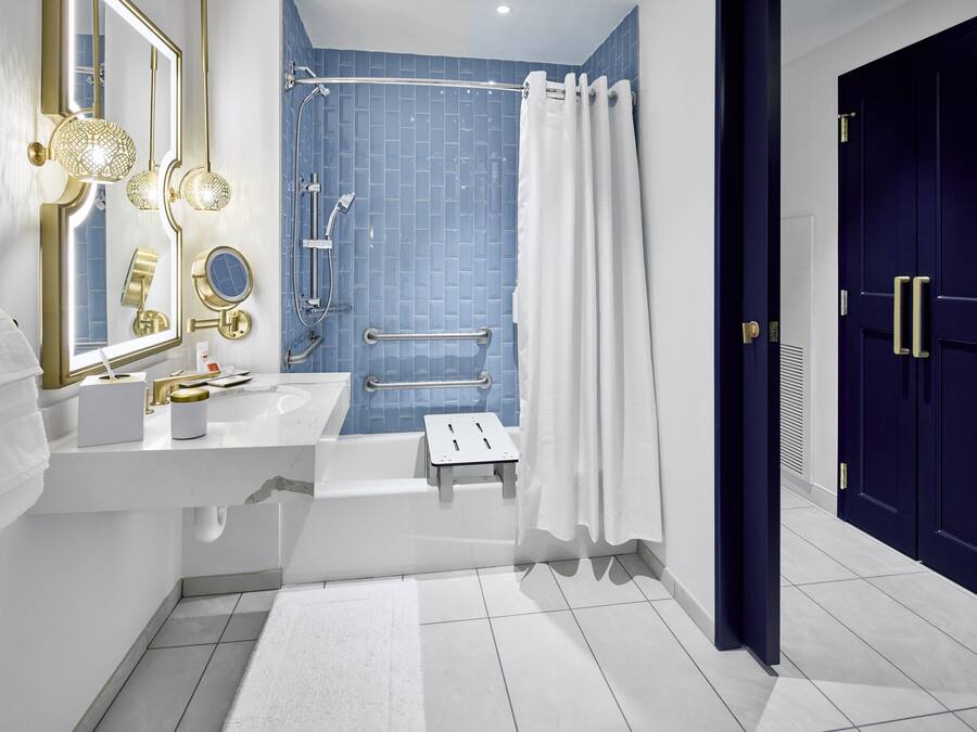 Un baño moderno con un lavamanos blanco, un espejo grande, una ducha con azulejos azules y una puerta azul oscuro.