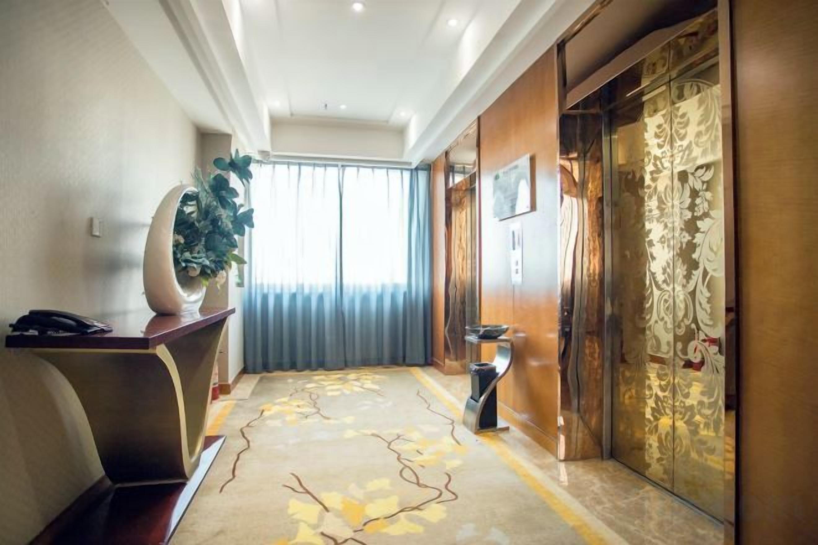 Un hall de hotel con una recepción, una planta grande en maceta, un tapete decorativo y una puerta de madera tradicional.
