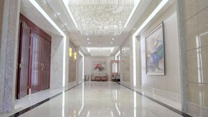 A spacious, well-lit hallway with marble floors, a chandelier, and framed artwork on the walls.