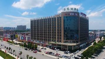 Hotel de varios pisos con fachada moderna de vidrio, situado en una intersección urbana con estacionamiento visible y edificios circundantes.