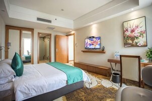 Habitación de hotel con una cama, televisión, un cuadro y un escritorio con una silla.