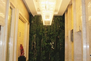 A hallway with a chandelier, a decorative statue, and a wall with vertical greenery. - Qinqingshu Hotel (Zhumadian)