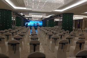 Un salón de conferencias con filas de sillas, un escenario con una pantalla grande y una araña de cristal.