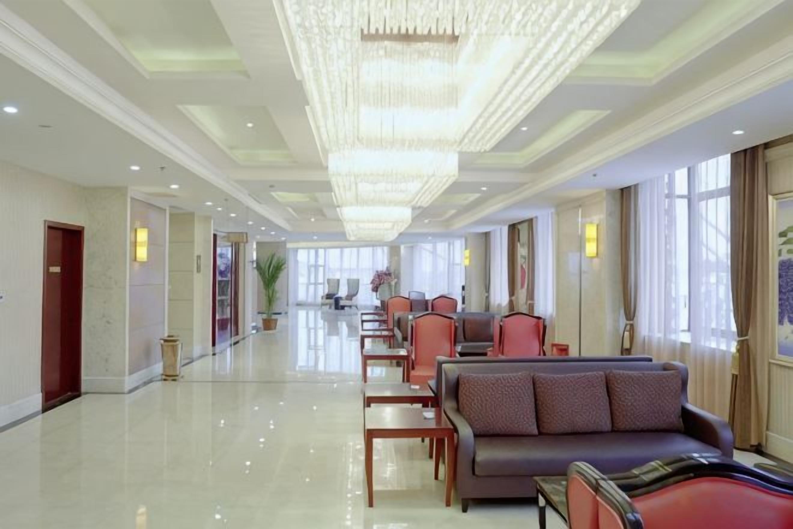 A hotel lobby with a long reception desk, seating area, and a chandelier.