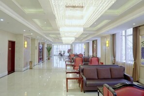 A hotel lobby with a long reception desk, seating area, and a chandelier. - Qinqingshu Hotel (Zhumadian)