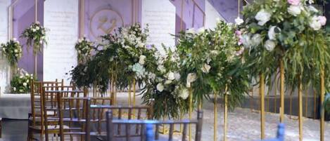 A venue with rows of wooden chairs, floral centerpieces, and a purple backdrop.