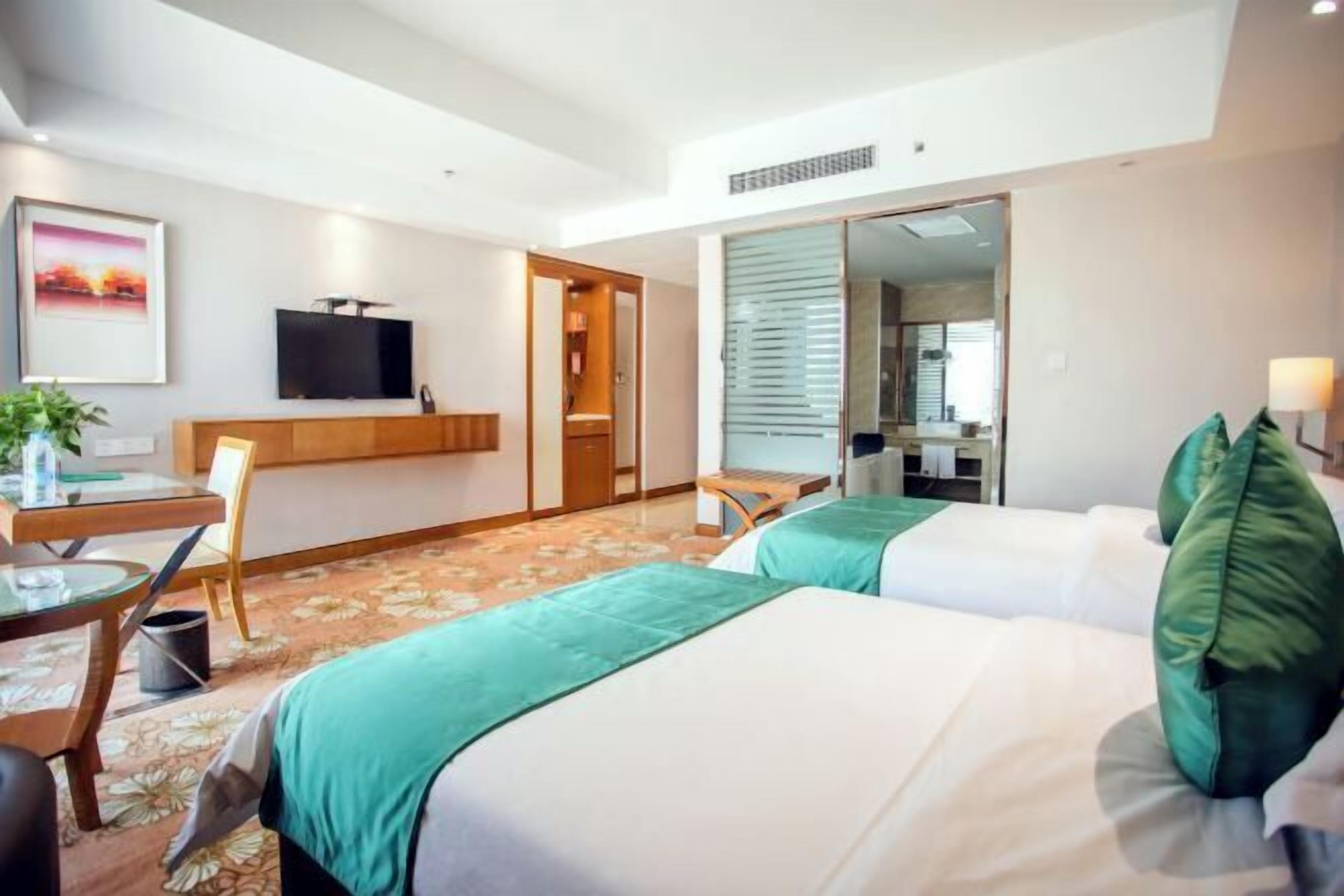 Habitación de hotel con dos camas, un escritorio con una silla, televisor y un espejo grande.