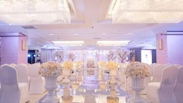 Un espacio para eventos formales con una larga mesa, sillas blancas y centros de mesa florales.