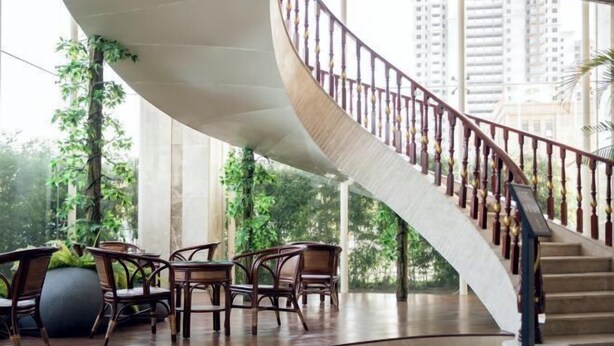 A curved staircase with a wooden railing, surrounded by indoor plants and furniture.