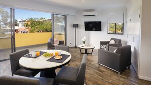 A modern living room with a round dining table, grey sofas, and a flat-screen TV mounted on the wall.