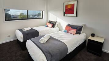 A hotel room with two beds, a nightstand, a framed picture, and a window with a city view.