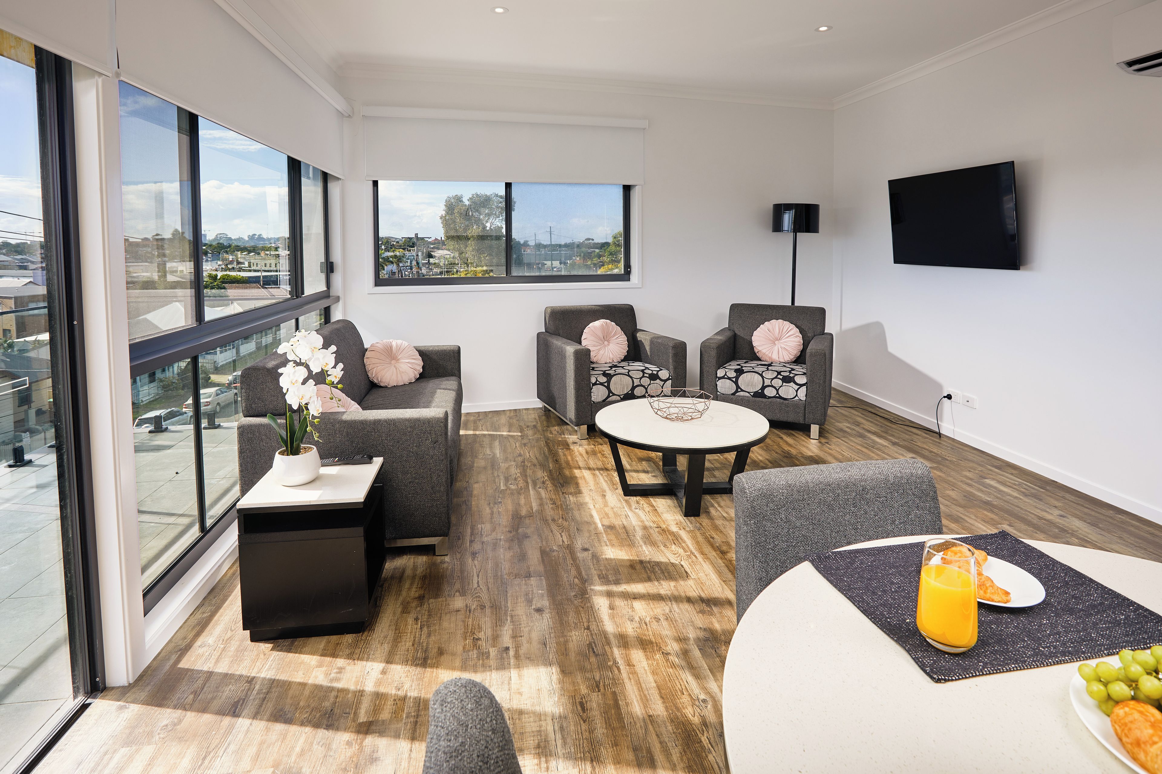 A modern living room with large windows, a flat-screen TV, and a dining area with a table and chairs.