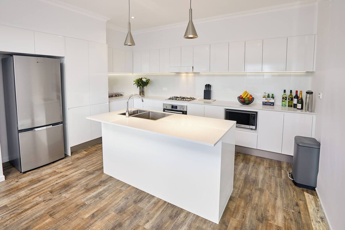 A modern kitchen with white cabinetry, a central island, stainless steel appliances, and a wooden floor.