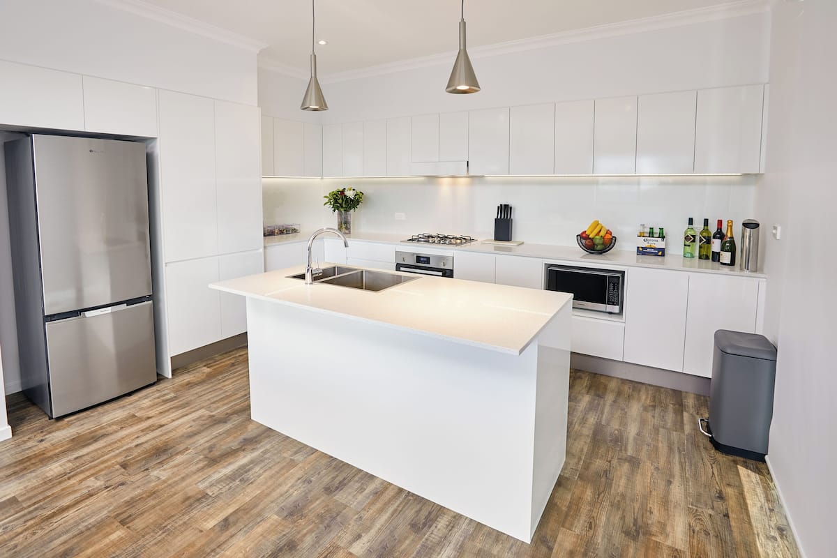 A modern kitchen with white cabinetry, a central island, stainless steel appliances, and a wooden floor.