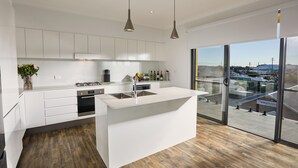 A modern kitchen with white cabinetry, a central island, and a large window offering a view of the outside.
