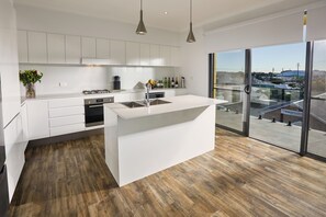 A modern kitchen with white cabinetry, a central island, and a large window offering a view of the outside.