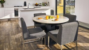 A modern kitchen with white cabinets, a dining area with a round table, and chairs. There is a view of the city through large windows.