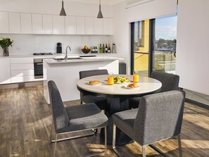 A modern kitchen with white cabinets, a dining area with a round table, and chairs. There is a view of the city through large windows.