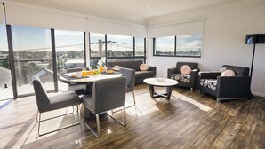 A modern living room with a dining area, large windows, and a city view. - Nouveau Serviced Apartments (Newcastle)