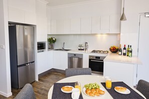 A modern kitchen with white cabinets, stainless steel appliances, and a breakfast setup on the dining table.
