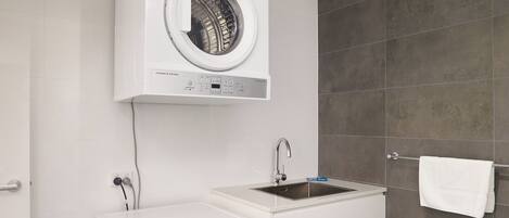 A compact laundry room with a front-loading washer and dryer, a sink, and a towel rack.