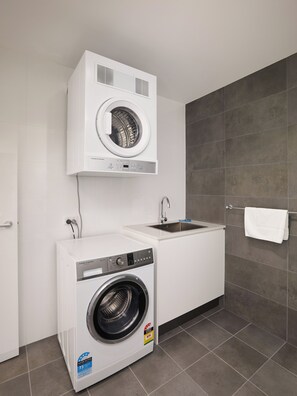 A compact laundry room with a front-loading washer and dryer, a sink, and a towel rack.